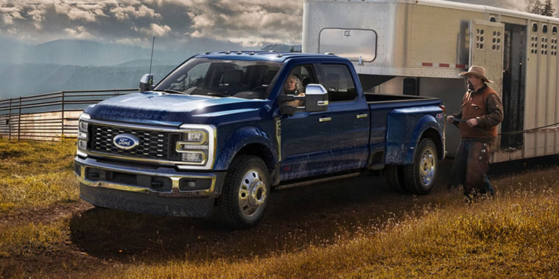 Blue heavy-duty pickup truck towing a horse trailer in a field.