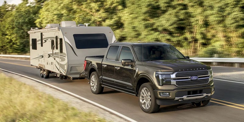 a 2025 Ford F-150 driving up a road pulling a trailer